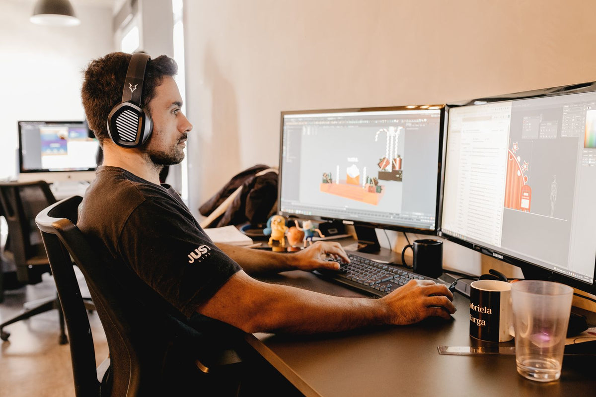 A developer in headphones building a game level on two monitors